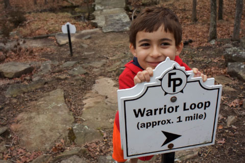 A little boy smiling by the trial sign for the Warrior Loop