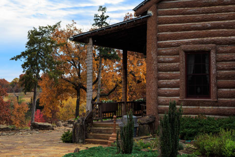 The porch of the Woolaroc lodge with fall foliage behind it