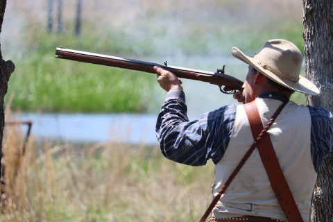 A mountain man shooting a rifle at Woolaroc