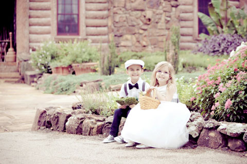 A ringbearer and flowergirl sitting on a rock wall during a wedding ceremony at Woolaroc