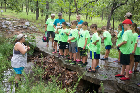 A Woolaroc volunteer teaching school children about nature while they explore a creek